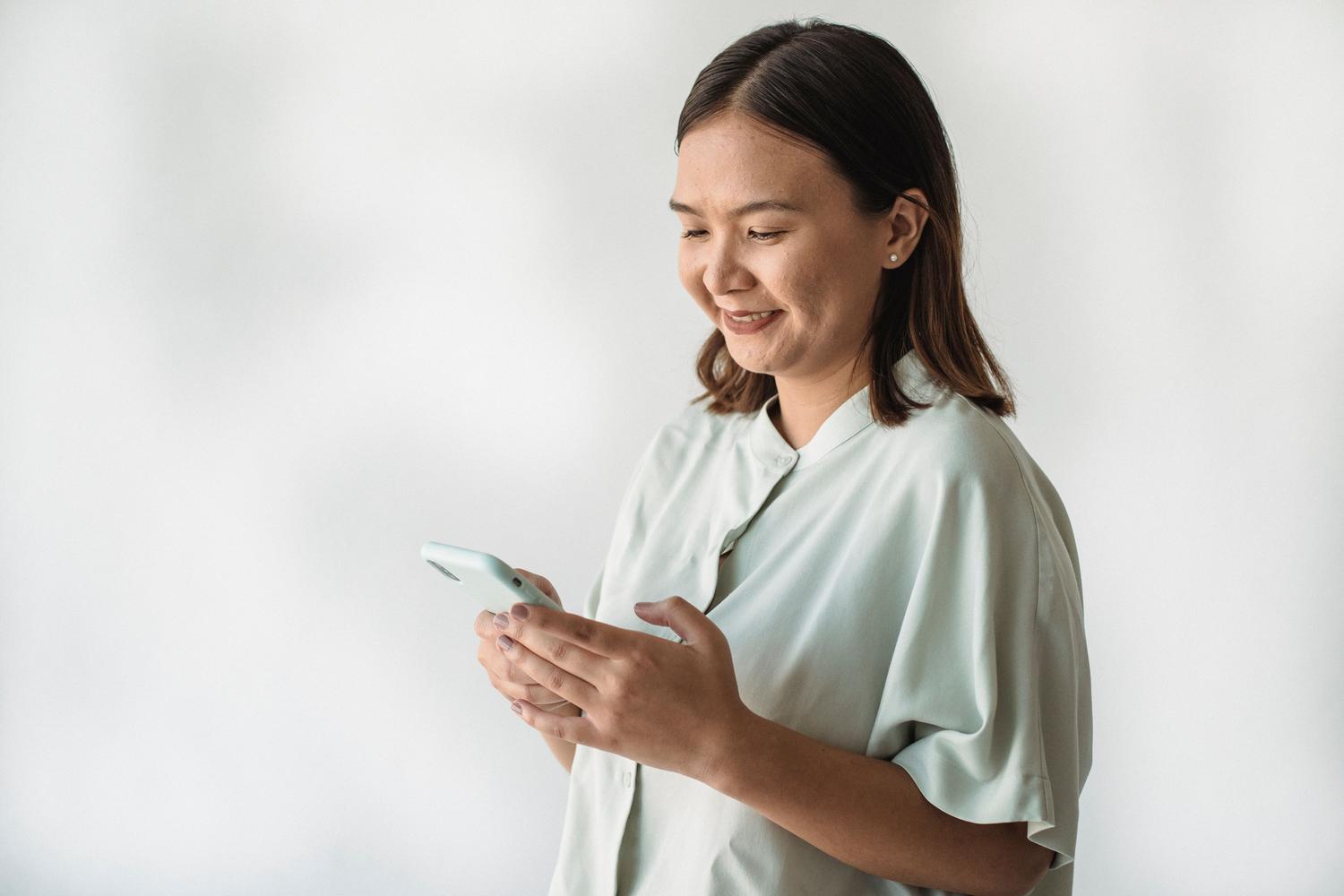 Mujer sonriente utilizando su teléfono móvil en interiores, representando la fase de búsqueda y chat en Facebook Dating.