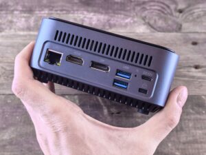 Mini PC compacto sostenido en la mano mostrando puertos traseros