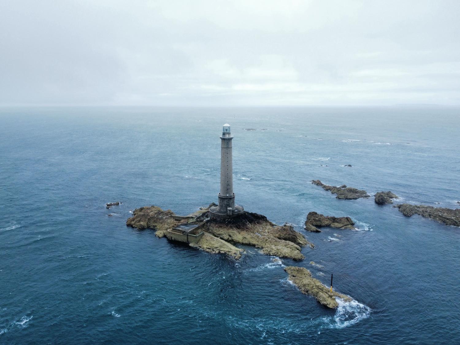 Faro solitario sobre un afloramiento rocoso Faro solitario sobre un afloramiento rocoso en medio de un océano vasto y gris, simbolizando la soledad en un mundo devastado.
