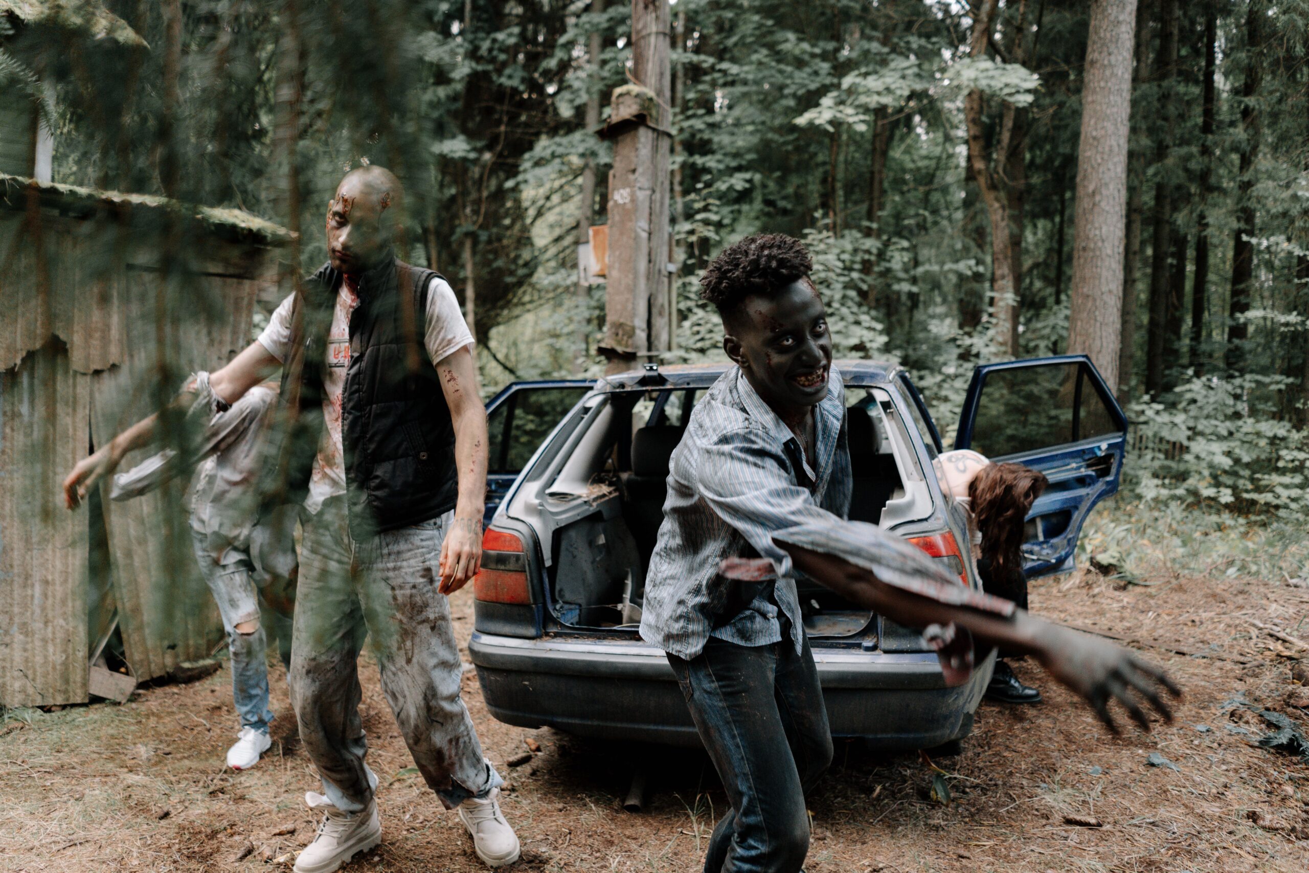 Horda de zombis caminando junto a un coche abandonado en un entorno oscuro y terrorífico.