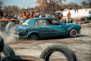 Coche BMW derrapando en tierra levantando polvo con espectadores al fondo, mostrando personalización y acción de carreras