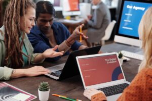 Equipo diverso de profesionales colaborando en una oficina moderna con laptops, discutiendo la evolución digital y el valor estratégico humano en la automatización.