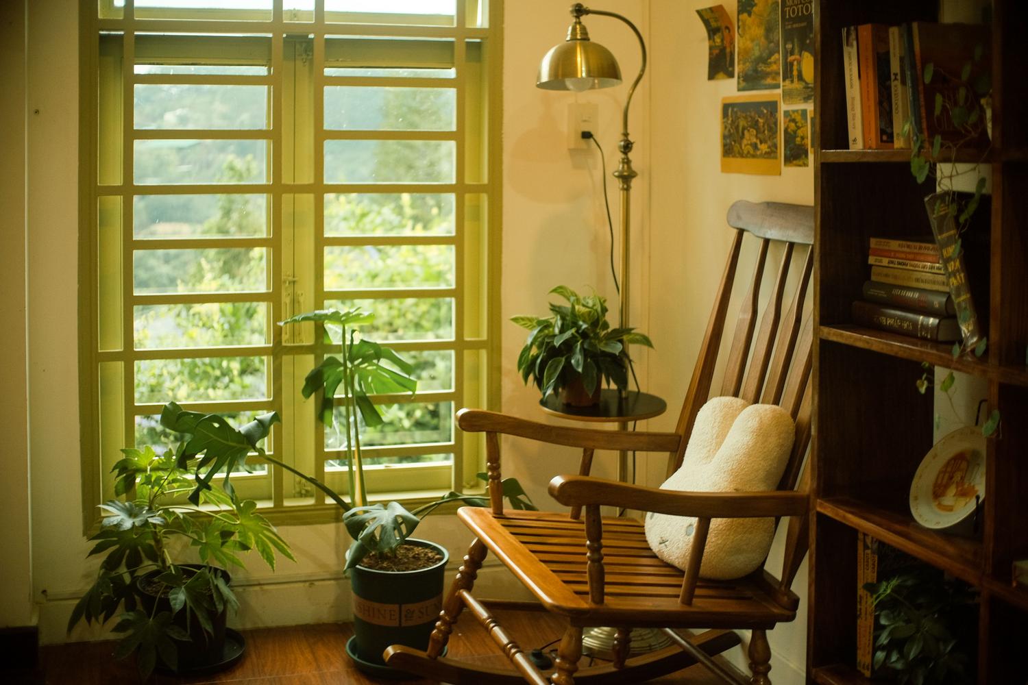 Rincón de lectura cálido con una mecedora de madera y plantas junto a la ventana, ideal para decorar el hogar virtual