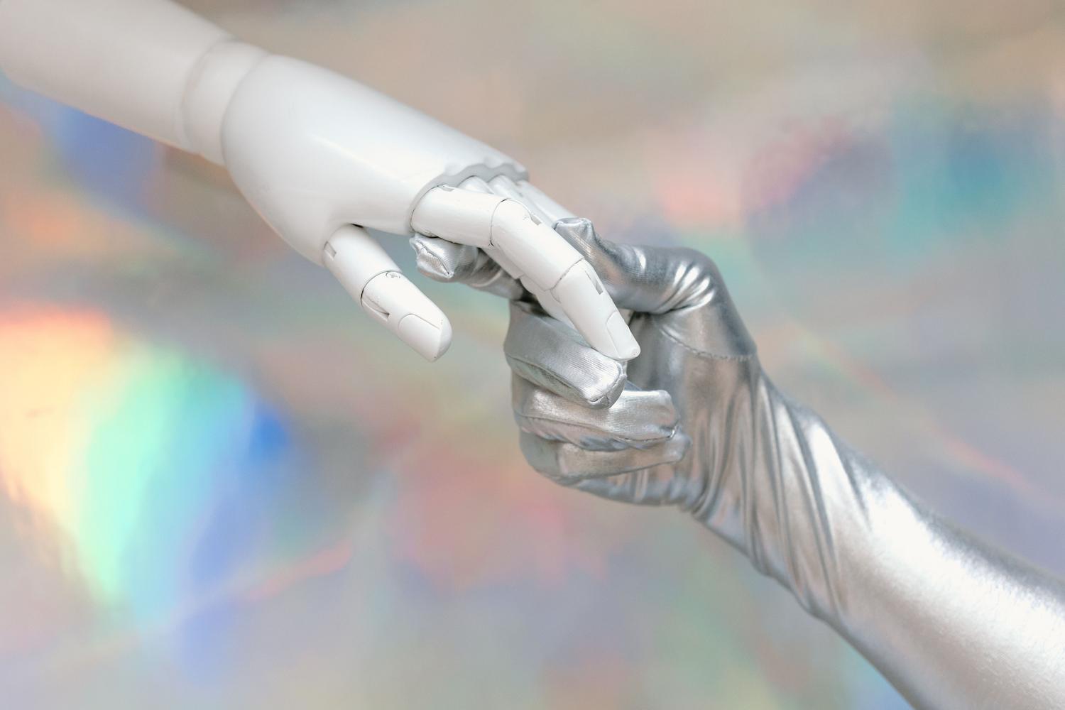 Encuentro entre una mano humana y una mano robótica, simbolizando la colaboración humano-IA, la ética y la supervisión constante del sistema.
