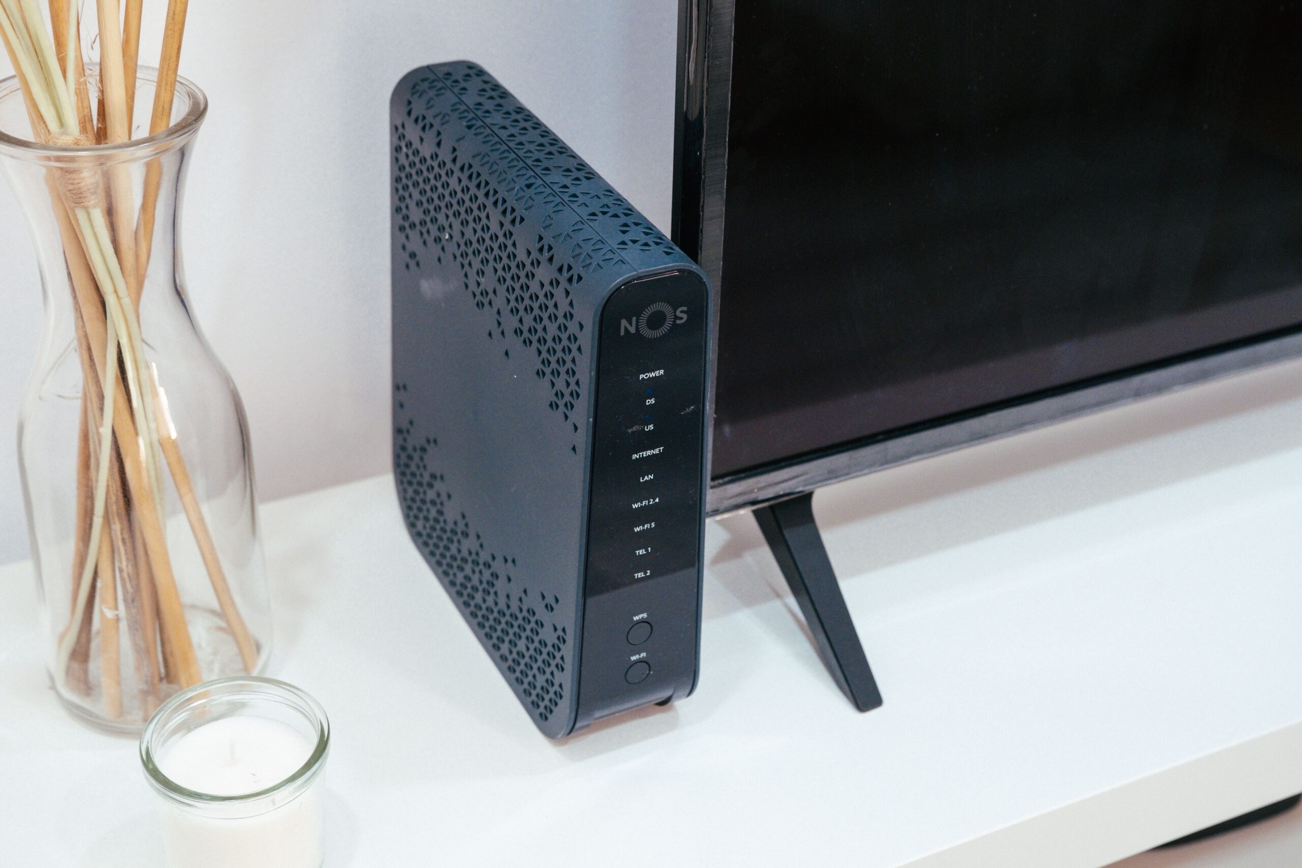 Configuración doméstica de red con un router negro sobre una mesa blanca junto a un monitor, ilustrando el entorno donde se instala una VPN en el router.