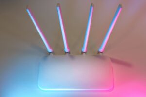 Router inalámbrico moderno de color blanco con cuatro antenas y luces decorativas en tonos azul y rosa, representando la tecnología de red avanzada.