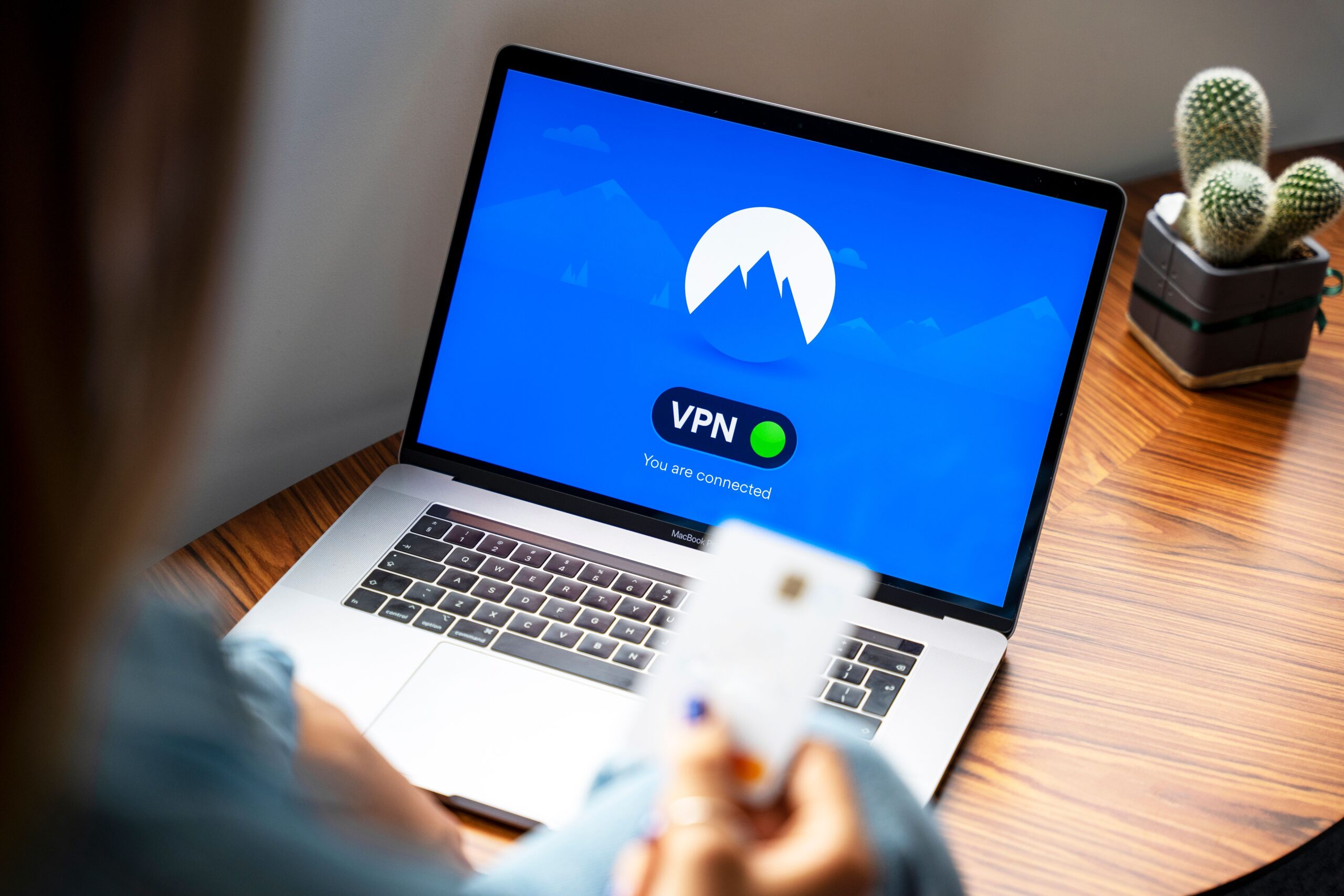 Primer plano de un portátil sobre una mesa de madera mostrando una aplicación de VPN conectada, ejemplificando la navegación segura y el cifrado de datos.