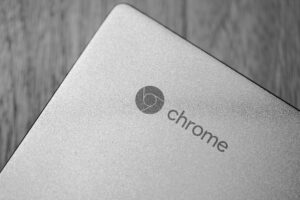 Primer plano en blanco y negro del logotipo de Chrome en la tapa de un portátil Chromebook, destacando el diseño minimalista y la identidad visual del dispositivo