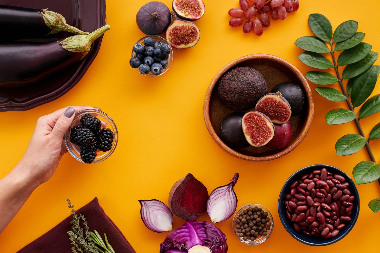 Variedad de frutas y verduras de colores intensos sobre fondo amarillo, ilustrando la importancia de consumir diversos fitoquímicos.