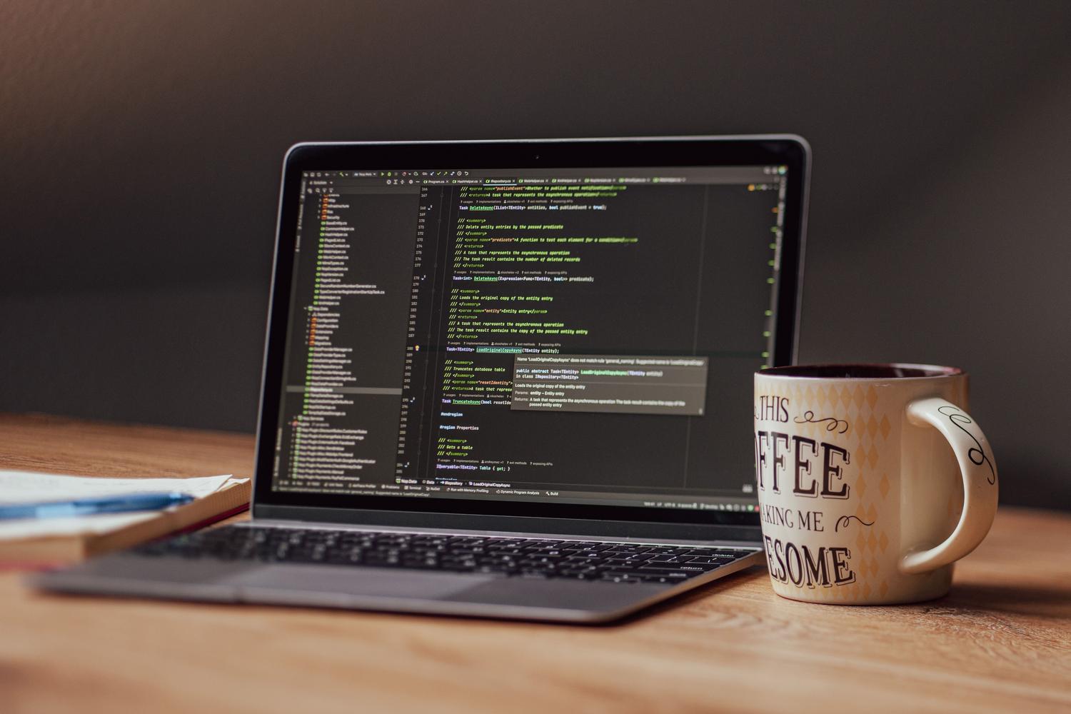Portátil con código y una taza de café sobre un escritorio, evocando la atmósfera de un desarrollador independiente creando herramientas de freeware o donationware.