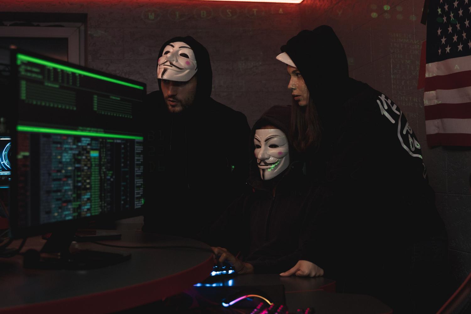 Hackers con capucha trabajando en un ordenador en un entorno oscuro, simbolizando la amenaza de intrusión en cámaras IP.