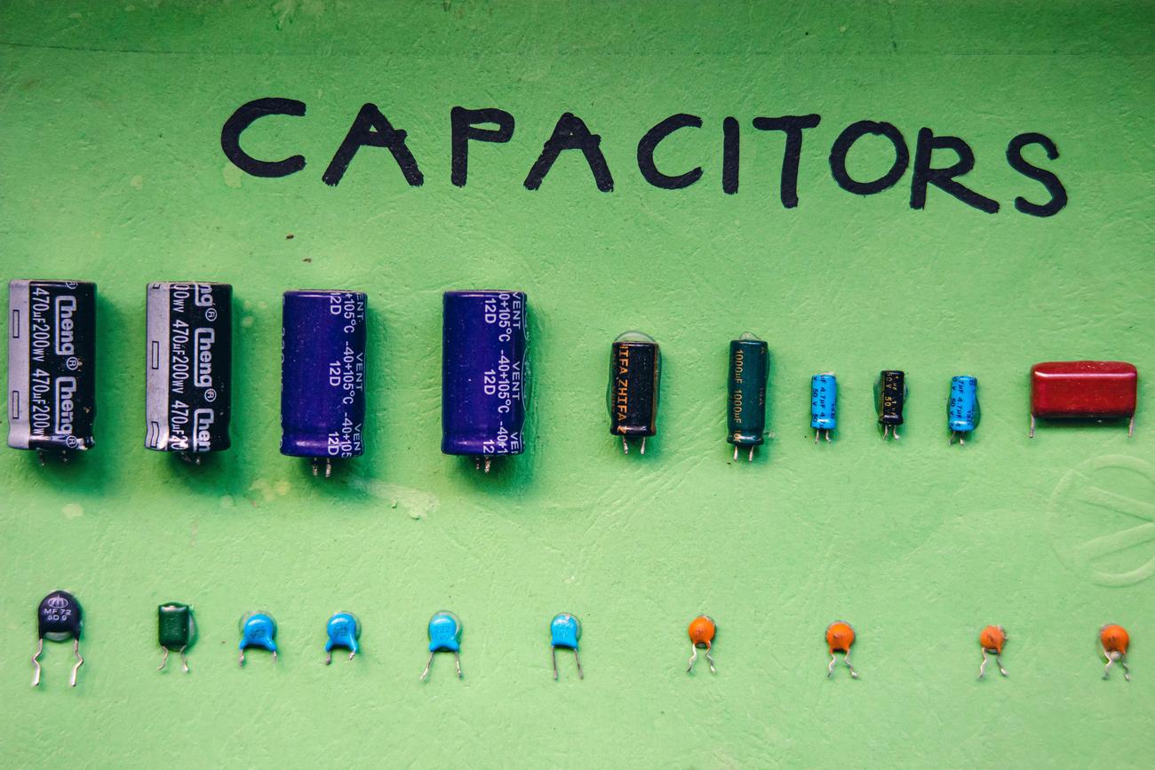 Diversos tipos de condensadores electrolíticos y cerámicos organizados sobre un fondo verde para ilustrar la capacitancia.