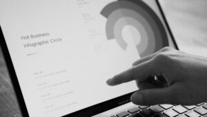 Mano señalando una infografía circular de negocio en la pantalla de un portátil, en tono blanco y negro, representando la creación de diagramas visuales con tecnología