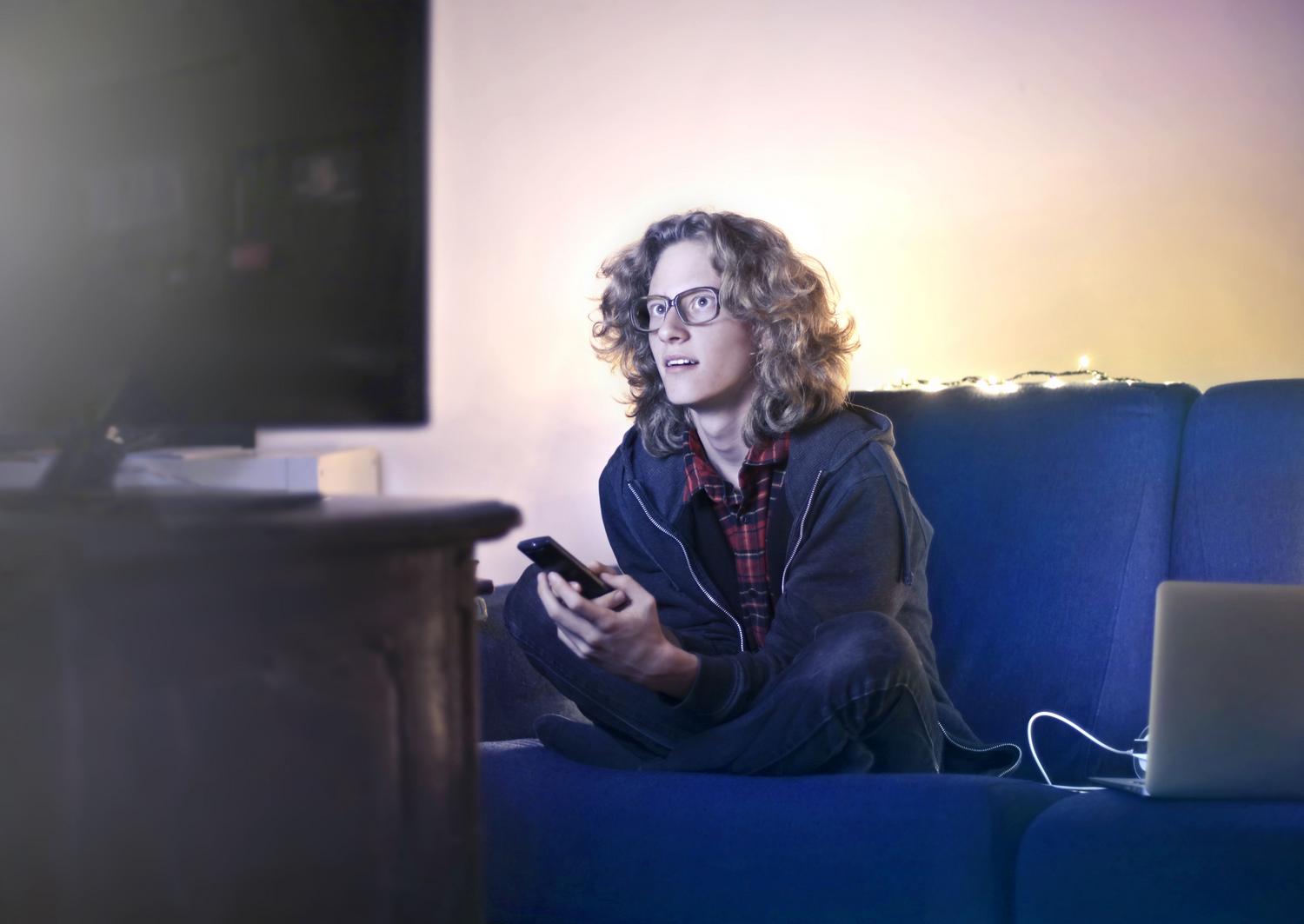 Hombre utilizando su smartphone mientras ve la televisión, ilustrando la sincronización entre el móvil y Google TV