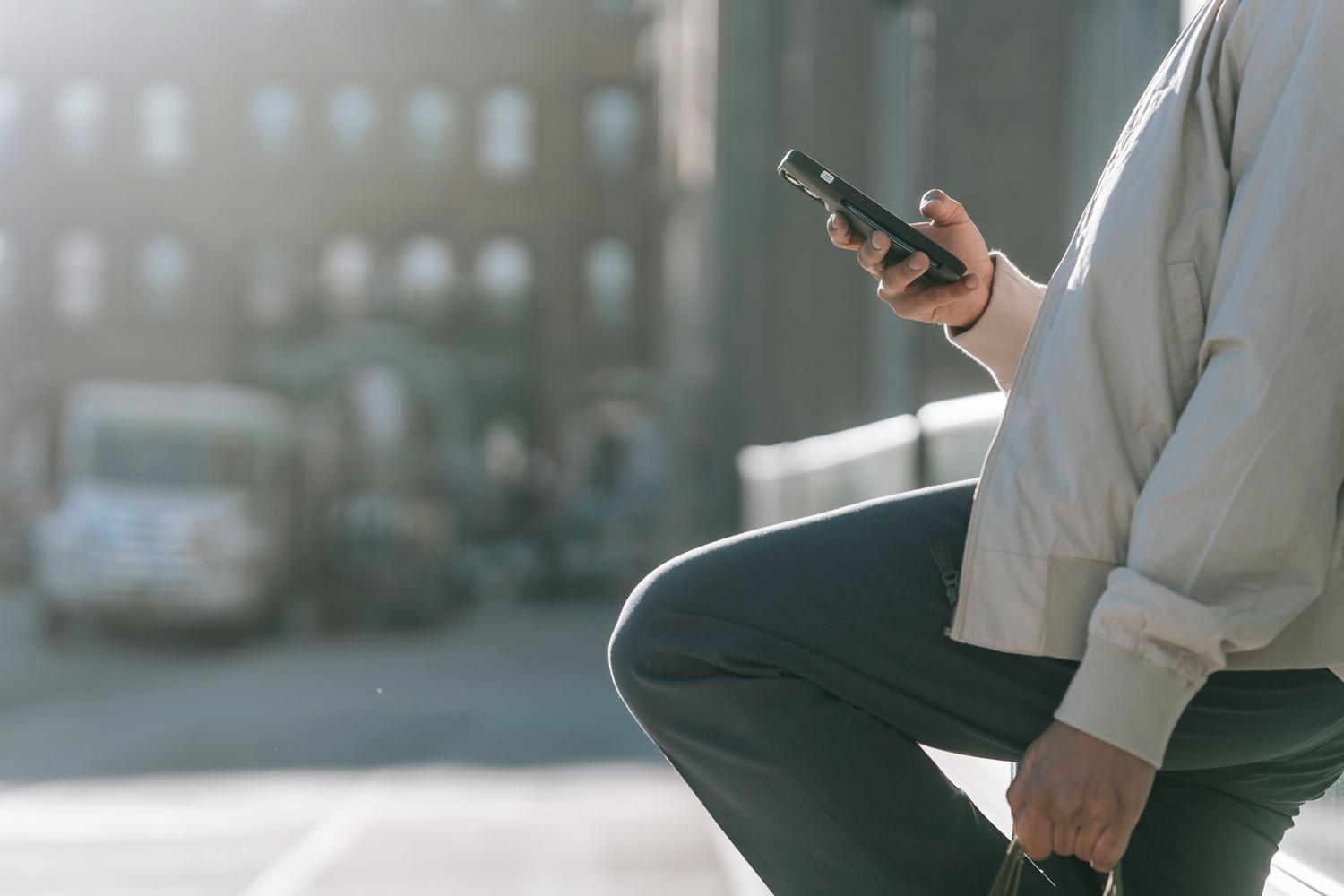 Persona utilizando un smartphone moderno en un entorno urbano luminoso, ideal para ilustrar la experiencia de usuario con iOS 26.