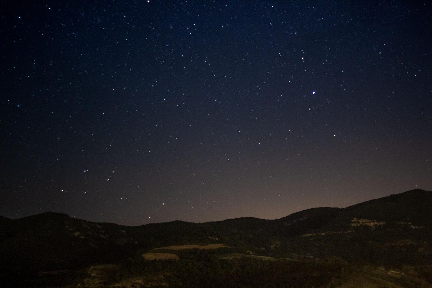 Cielo nocturno estrellado sobre un paisaje de montañas, haciendo referencia a la observación de las estrellas y al título de la obra.