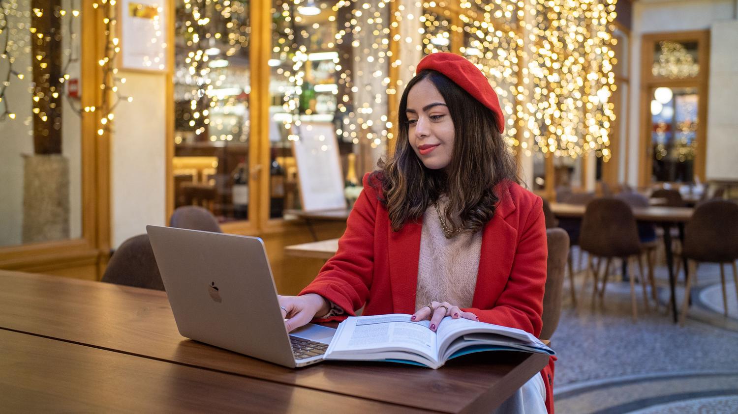 Estudiante concentrada estudiando con su ordenador portátil en una cafetería europea, ilustrando los espacios alternativos de estudio y concentración.