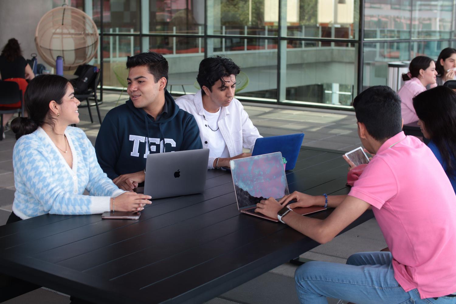 Jóvenes adultos de diversas nacionalidades colaborando con ordenadores portátiles al aire libre, simbolizando la movilidad estudiantil y la inmersión cultural.