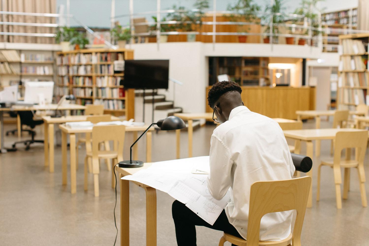 Estudiante trabajando en un escritorio dentro de una biblioteca moderna y luminosa, representando el 'lugar sagrado del silencio' para el estudio.