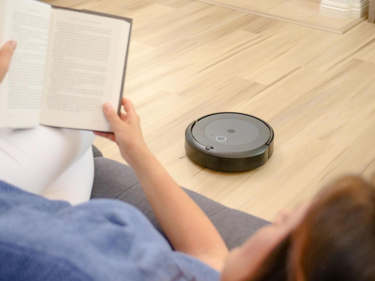Mujer relajándose en el sofá mientras un robot aspirador limpia el suelo de forma autónoma gracias al Smart Plan.