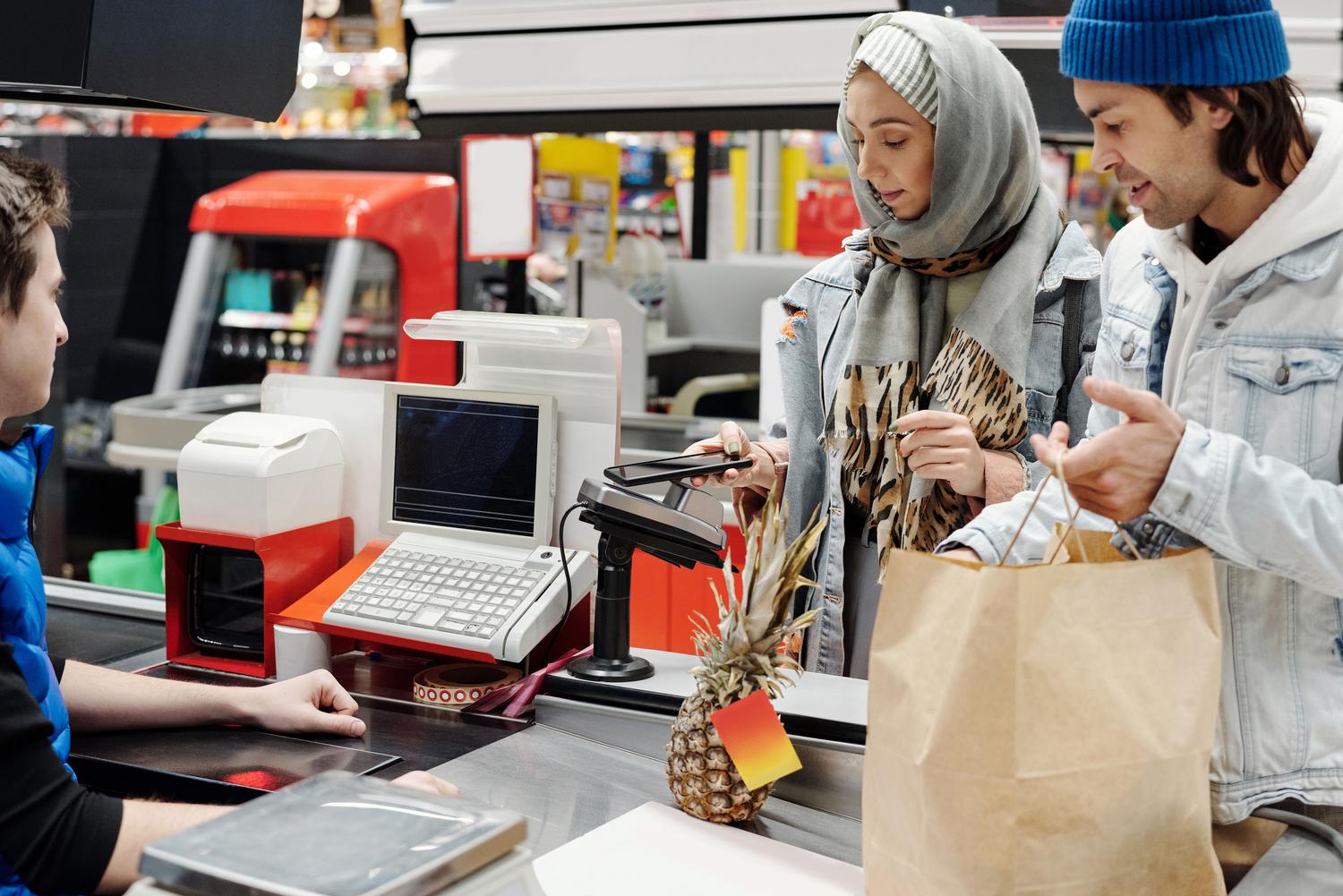 Una persona realizando un pago móvil con su smartphone en la caja de un supermercado, ilustrando la utilidad diaria de una SuperApp.