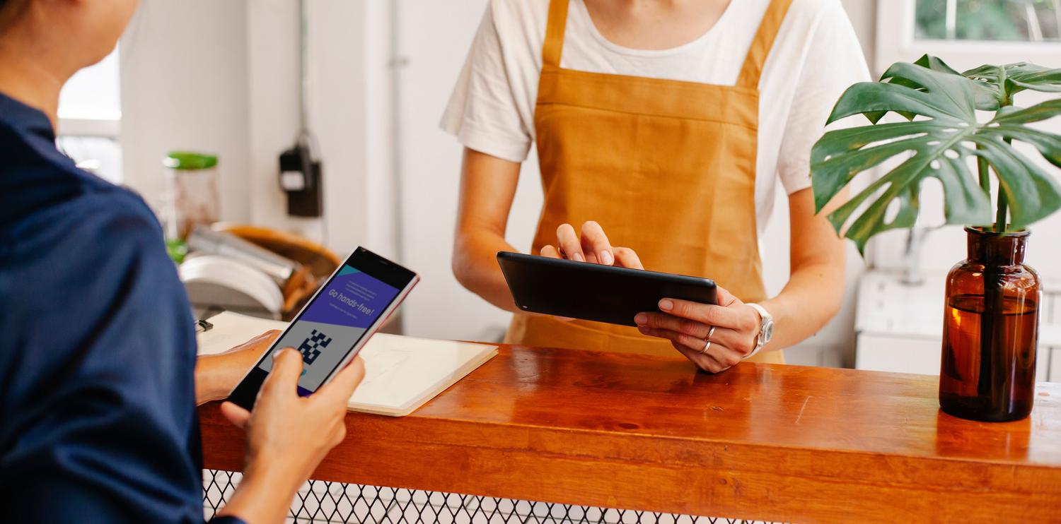 Interacción de pago digital en una cafetería, donde el cliente muestra un código QR en su móvil al vendedor.