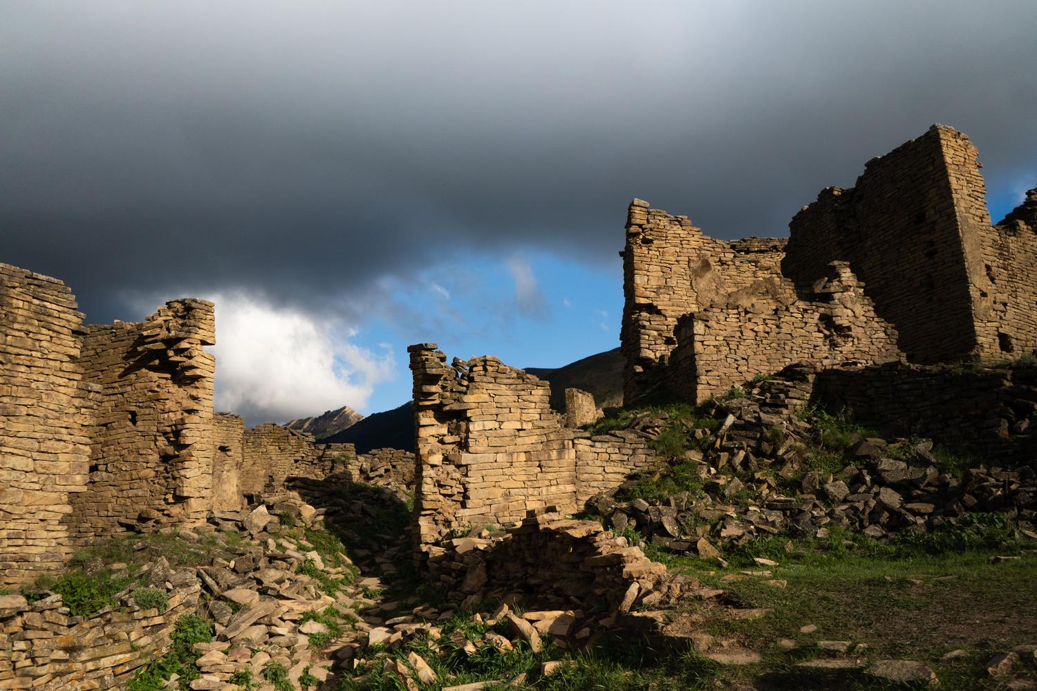 Ruinas de una fortaleza bajo un cielo tormentoso, evocando la atmósfera de fantasía oscura de Nodus Fall.