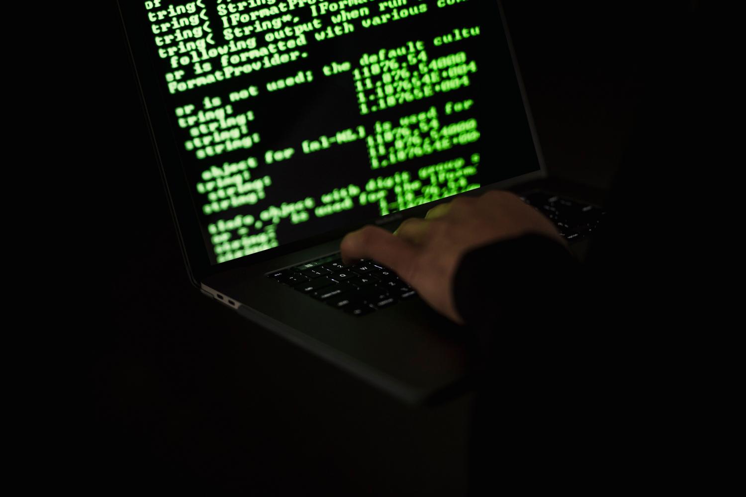 Primer plano de manos escribiendo código en un portátil con luz verde, simbolizando la creación y propagación de malware.