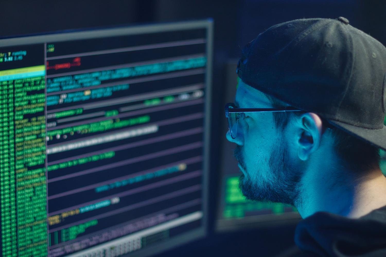 Experto en ciberseguridad analizando líneas de código complejas en múltiples monitores para detectar virus autorreplicantes.