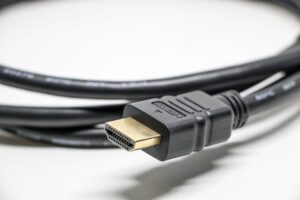 Primer plano de un cable HDMI negro con conectores dorados sobre fondo blanco, ideal para ilustrar la conectividad física.