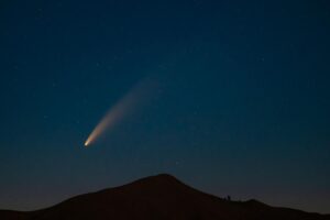 Un cometa brillante cruzando el cielo nocturno estrellado sobre la silueta de una montaña
