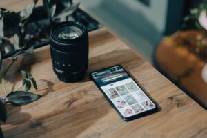 Bodegón creativo con un smartphone y un objetivo de cámara profesional sobre una mesa de madera, representando la fotografía móvil.