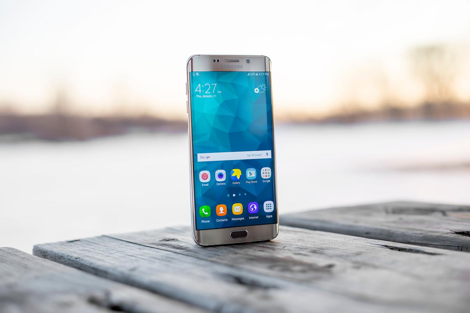 Smartphone Samsung apoyado sobre una superficie de madera al aire libre durante el atardecer.
