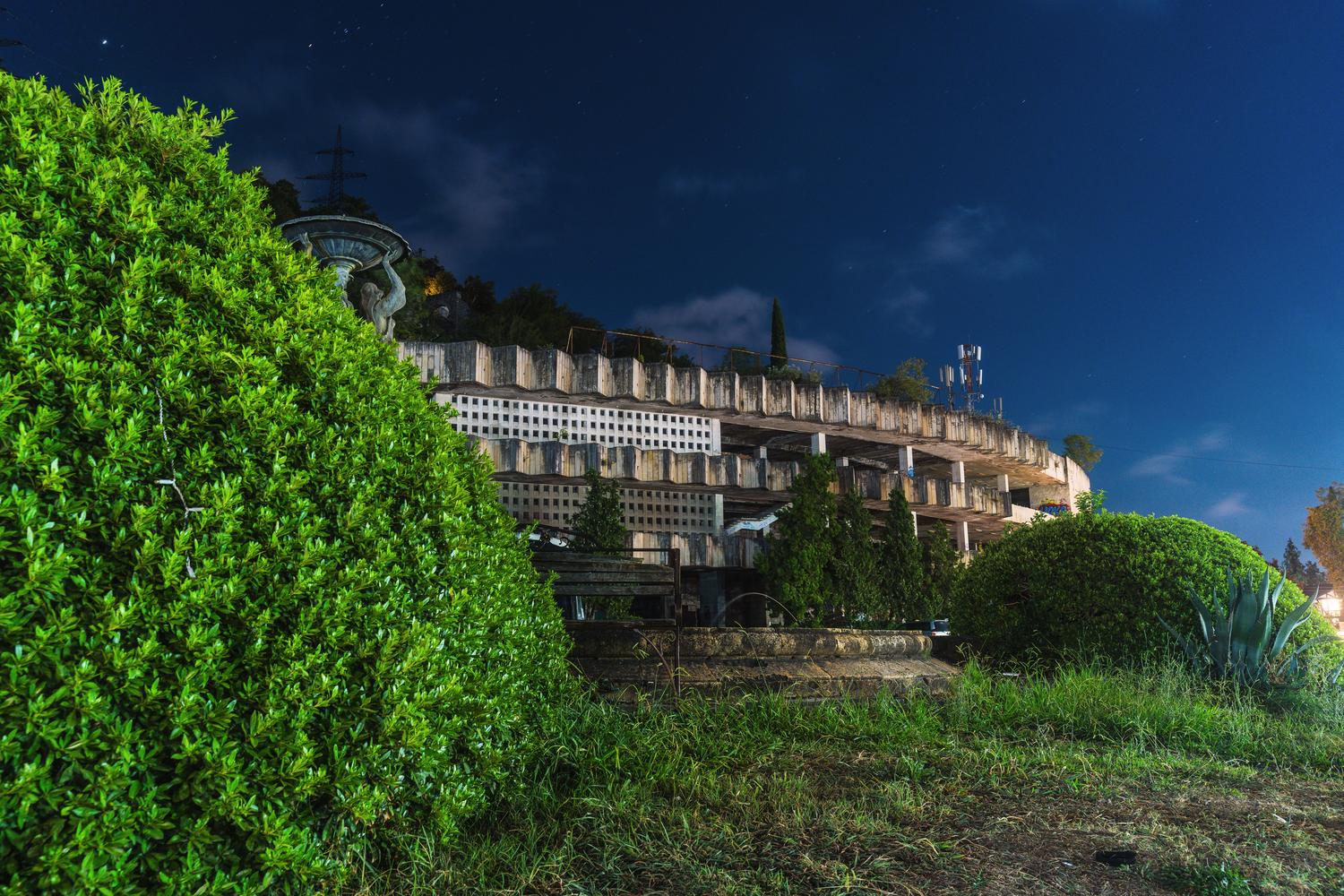 Edificio abandonado y decadente rodeado de vegetación tropical espesa durante la noche, creando una atmósfera de misterio y terror.