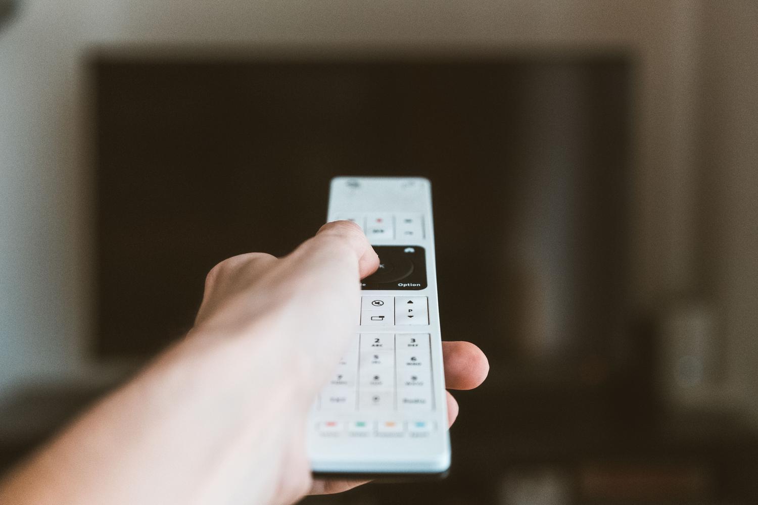 Primer plano de una mano utilizando un mando a distancia para sintonizar canales de televisión.