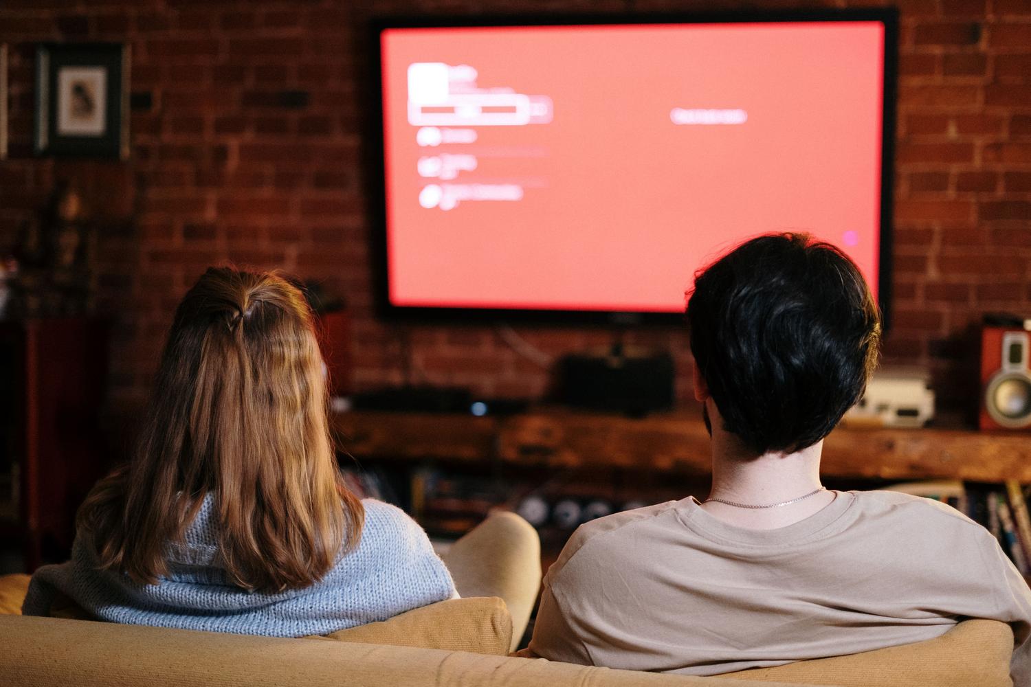 Pareja disfrutando de la televisión en un ambiente acogedor, representando el consumo de contenidos regionales y nacionales.