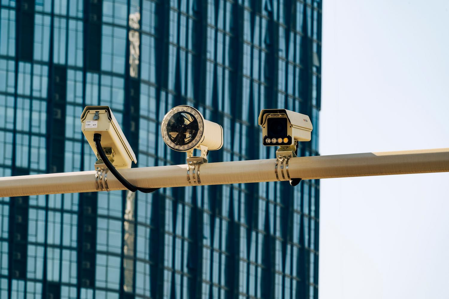 Cámaras de videovigilancia urbana montadas en un poste frente a un edificio moderno, ilustrando vectores de ataque en infraestructuras públicas.
