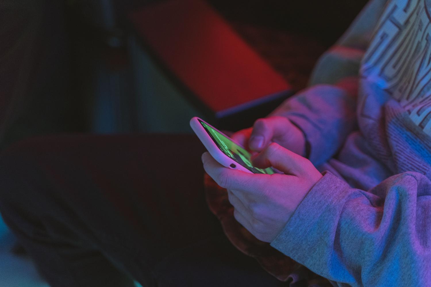Manos sosteniendo un smartphone con iluminación neón, capturando la estética y el ambiente gamer moderno.