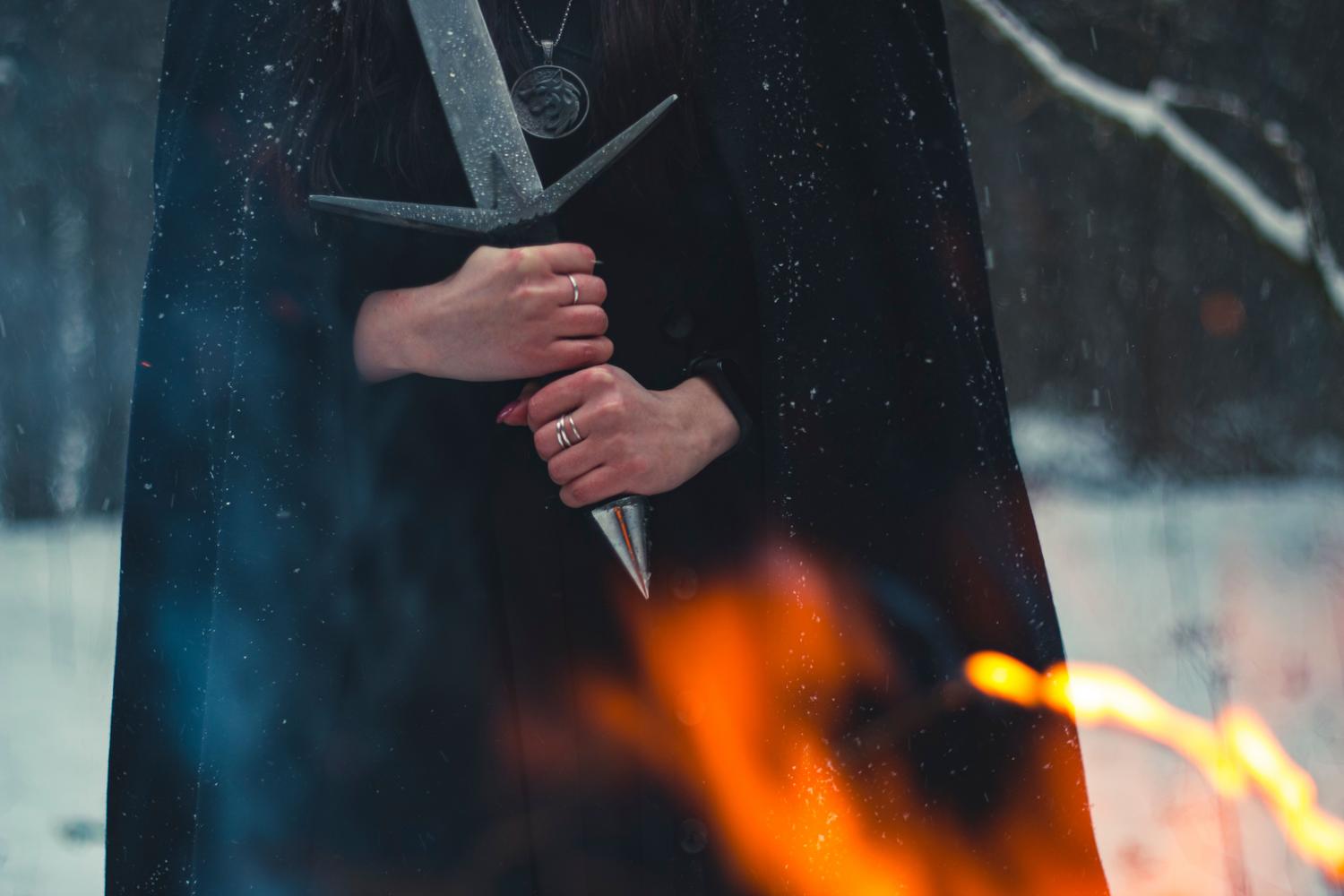 Figura misteriosa con espada entre la nieve y el fuego, representando los secretos y rutas arriesgadas del prólogo.