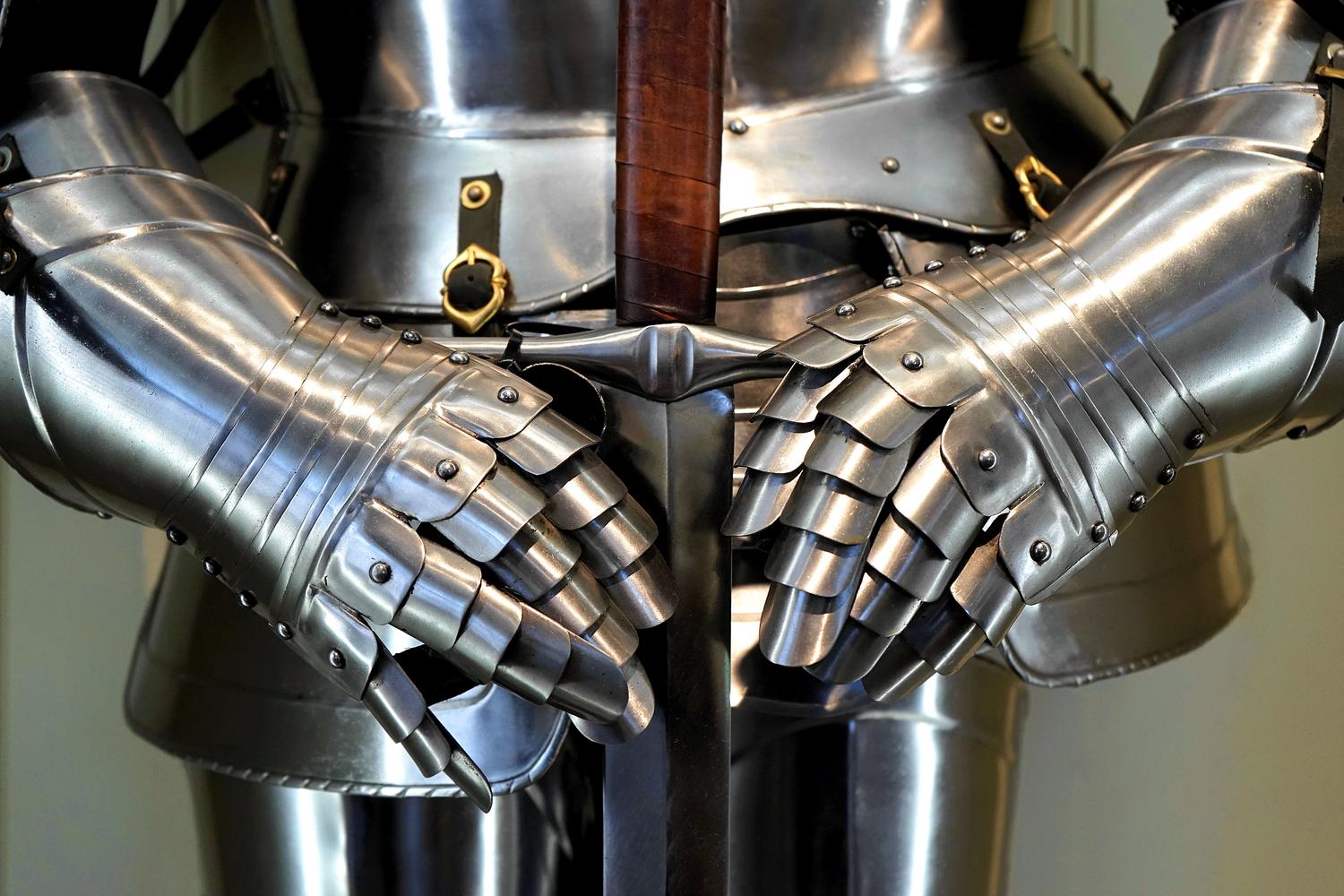 Detalle de guanteletes de armadura medieval sosteniendo una espada, representando el equipo y las estadísticas del personaje.