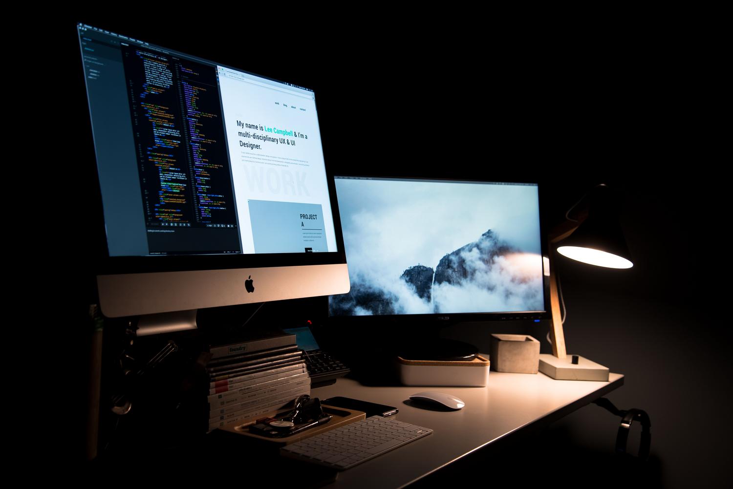 Workspace elegante con dos monitores, lámpara de escritorio y accesorios de oficina, representando un setup equilibrado.