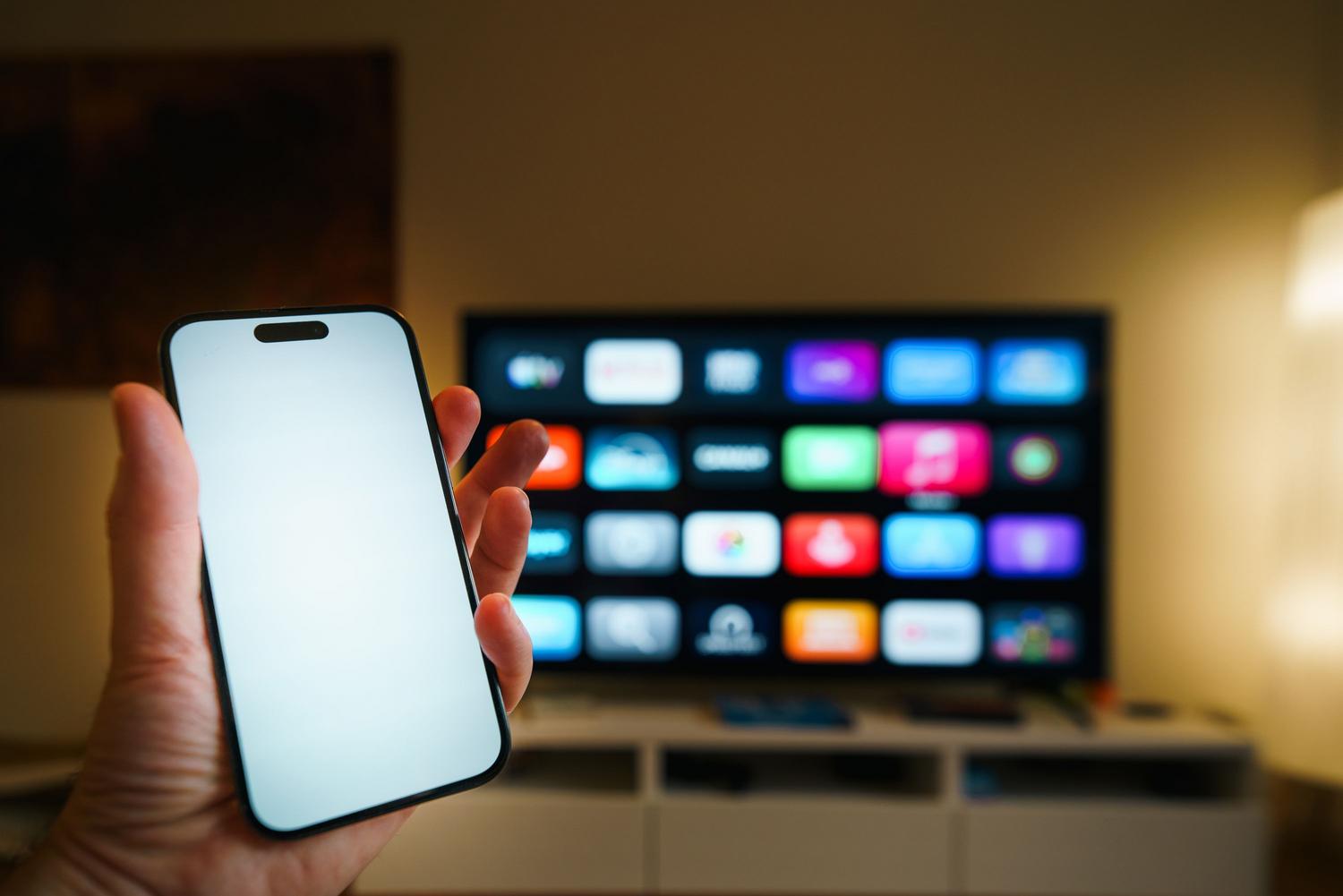 Persona utilizando un smartphone como mando a distancia para controlar una Smart TV en un salón acogedor.