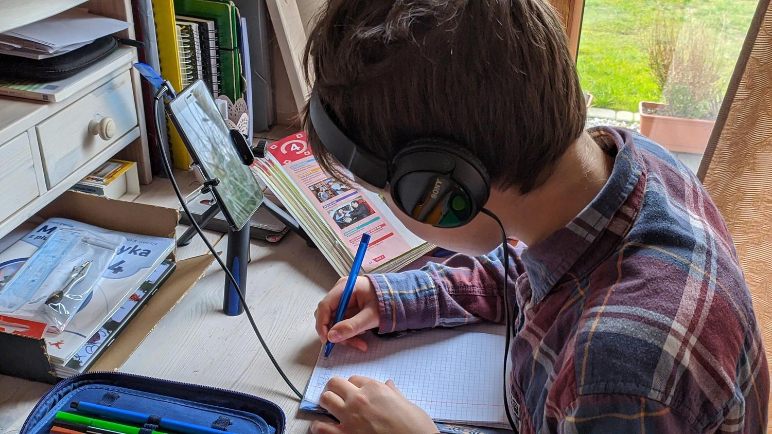 Niño tomando notas activamente en un cuaderno mientras usa la computadora, mostrando el uso de la tecnología como herramienta de aprendizaje