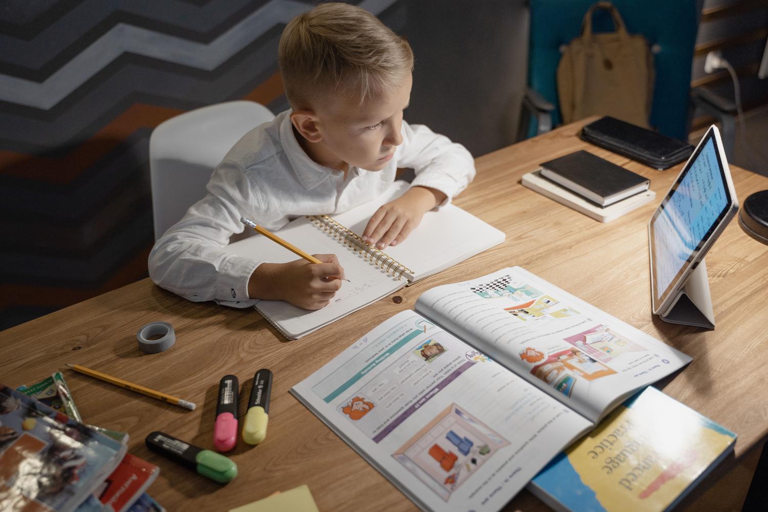 Niño concentrado estudiando con una tablet, libros y cuadernos sobre la mesa, representando el equilibrio entre lo digital y lo analógico