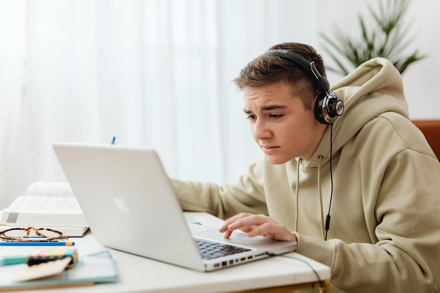 Adolescente con auriculares estudiando en línea con un portátil en un entorno acogedor, reflejando la productividad digital