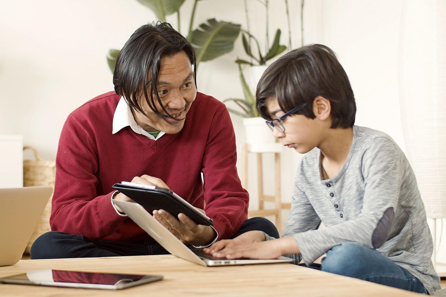 Padre e hijo interactuando con un portátil y una tablet, ilustrando la comunicación y guía parental en el uso de la tecnología