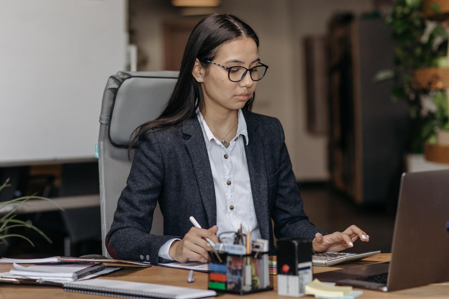 Profesional enfocada trabajando con su portátil y una calculadora, simbolizando el análisis de datos y la aplicación de fórmulas.