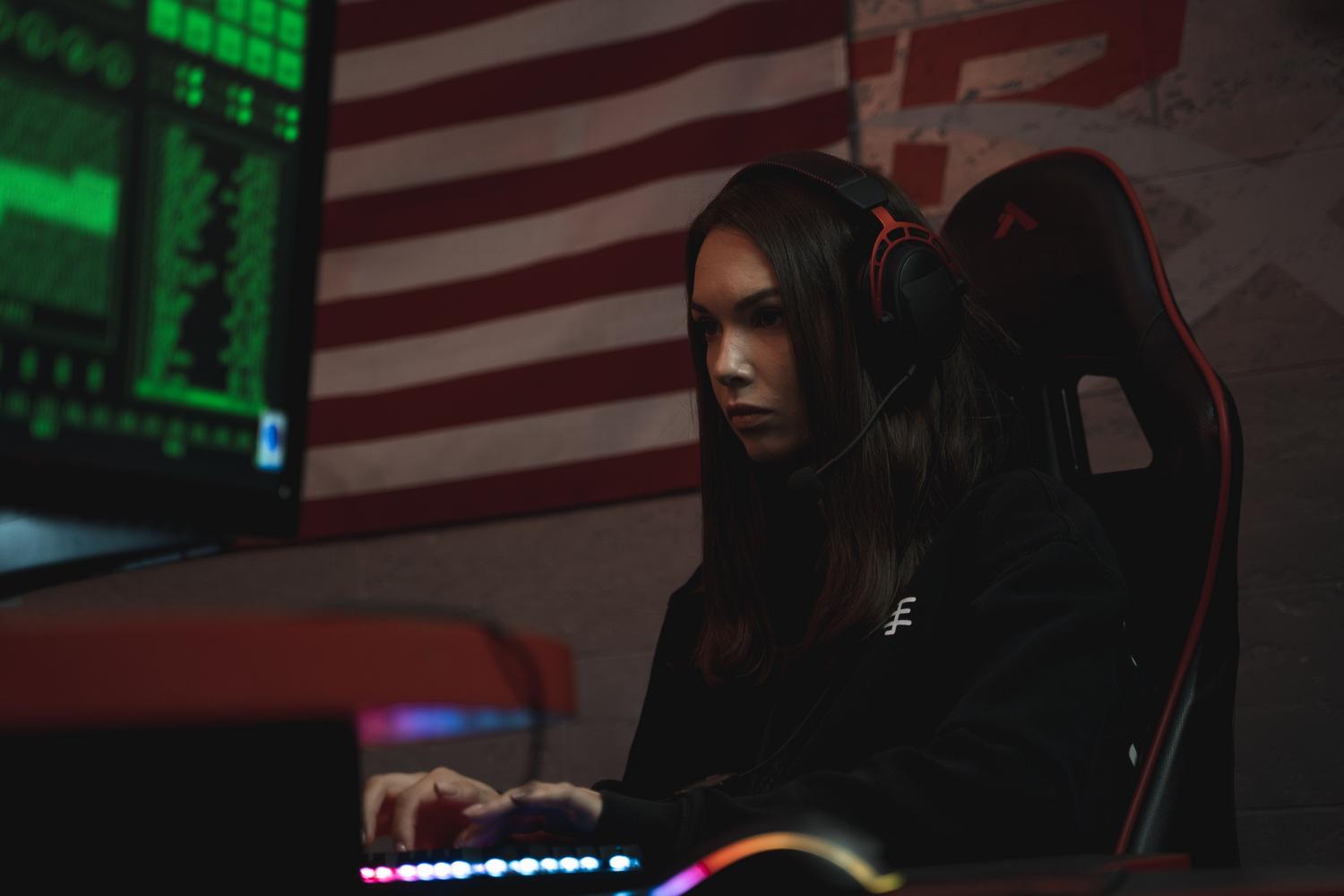 Mujer gamer concentrada frente al monitor usando auriculares profesionales en una habitación con iluminación neón.