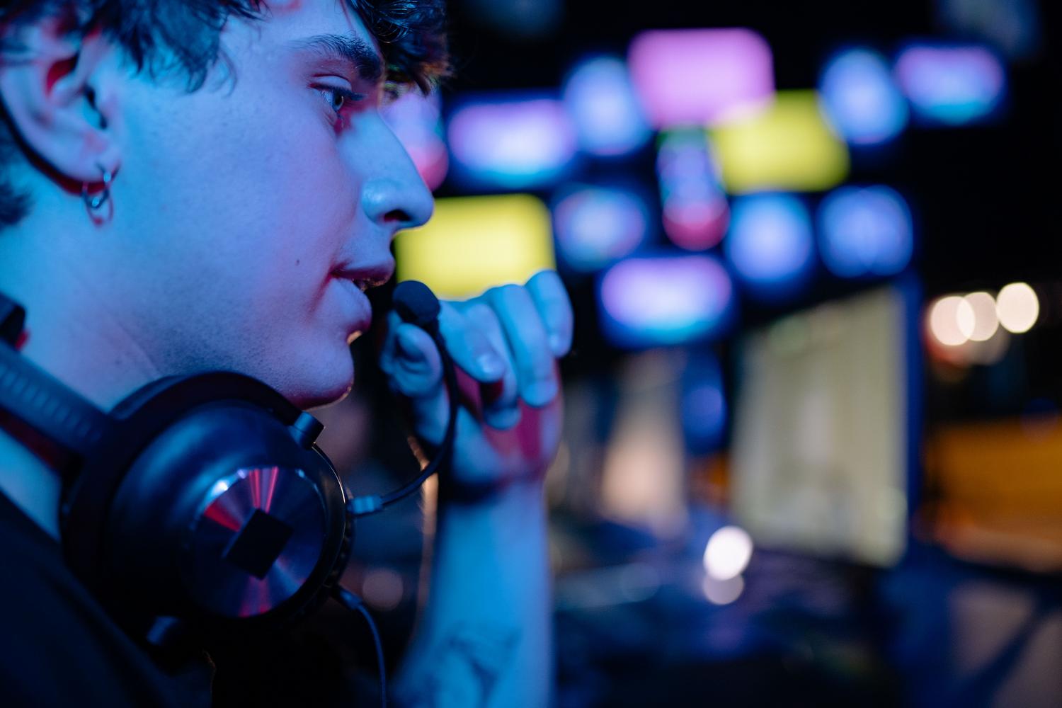 Primer plano de un gamer ajustando el micrófono de sus auriculares en un entorno de juego moderno con luces LED.