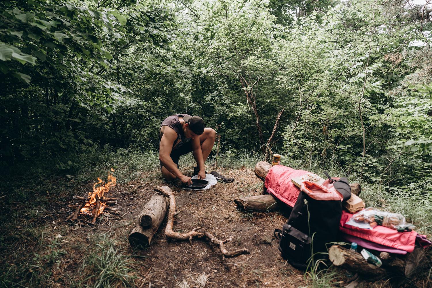Persona preparando equipo y fuego en la naturaleza, ilustrando la supervivencia y gestión de recursos de Palworld.